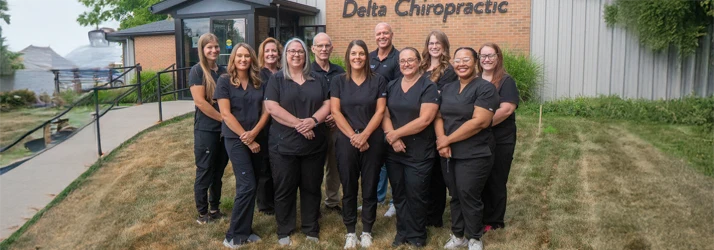 Staff members standing outdoors in front of a building with the "Delta Chiropractic" sign visible.